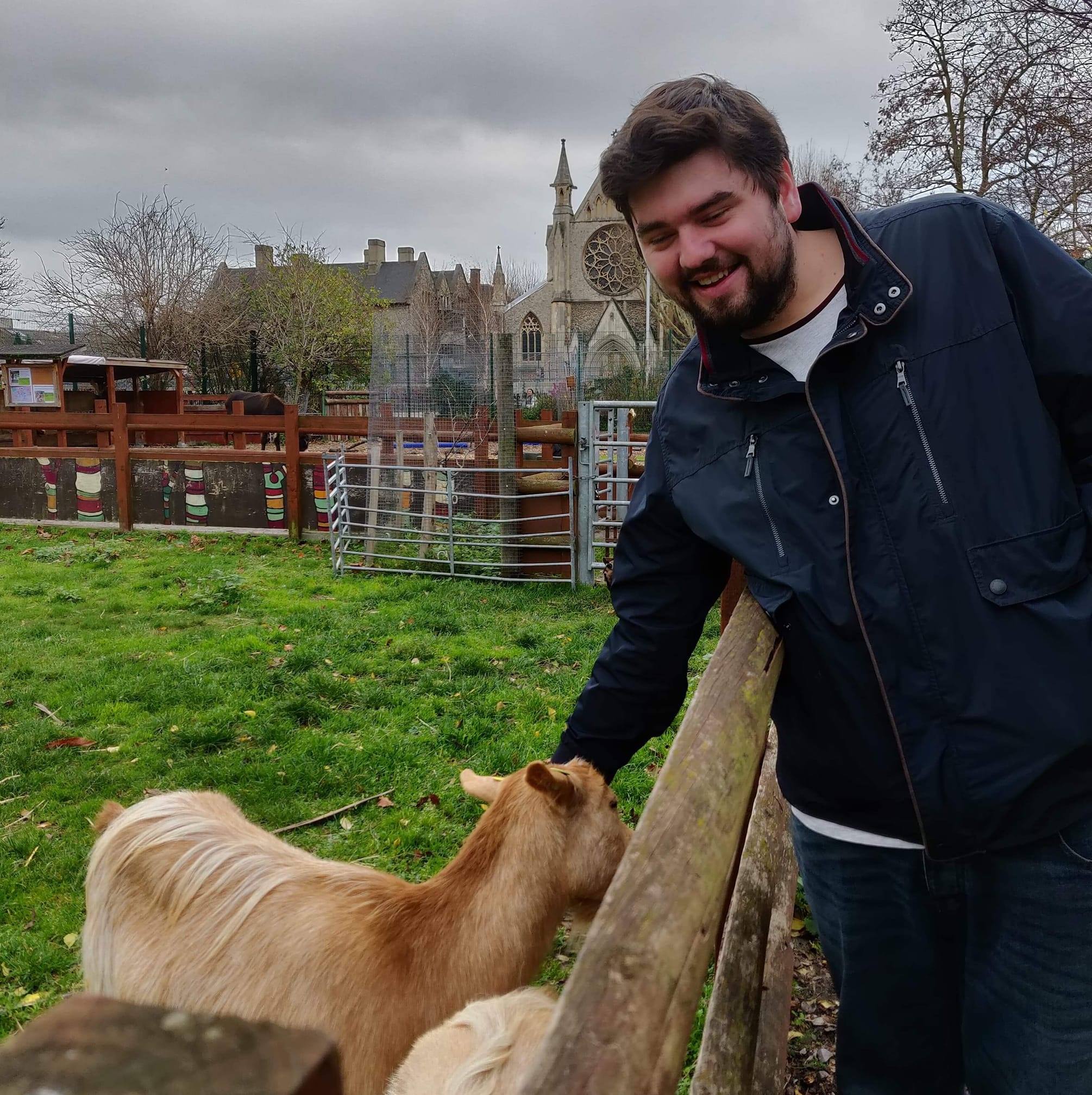 Aaron Pitty smiling in a navy jacket whilst petting a goat